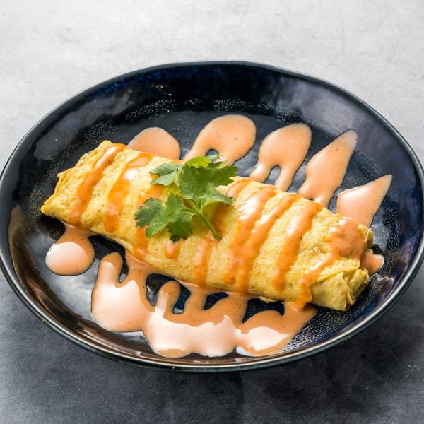 A golden omelet drizzled with orange sauce and garnished with cilantro on a dark plate.