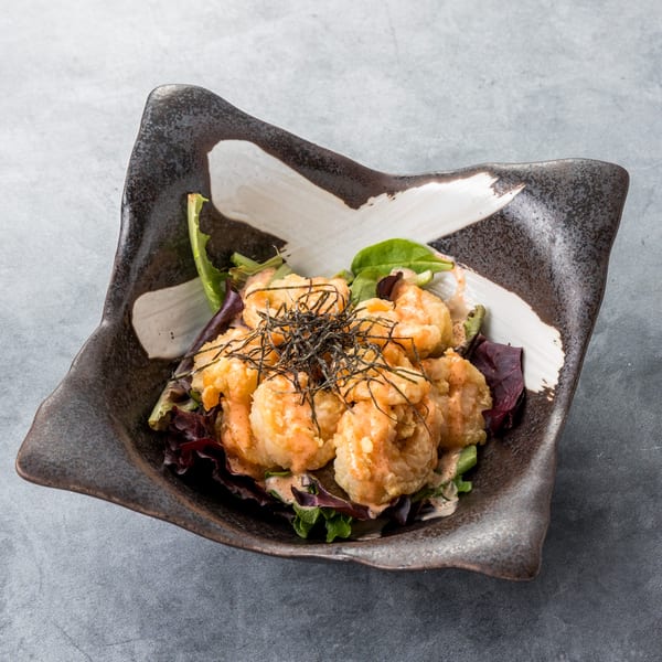 Crispy fried shrimp with sauce and seaweed on a bed of lettuce in a dark, square bowl.