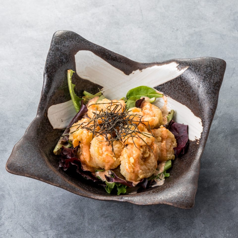 Crispy fried shrimp with sauce and seaweed on a bed of lettuce in a dark, square bowl.