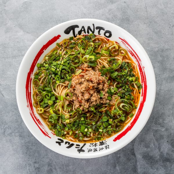 Tanto Gyoza and Ramen Bar's ramen bowl, topped with ground meat and green onions, on a gray surface.