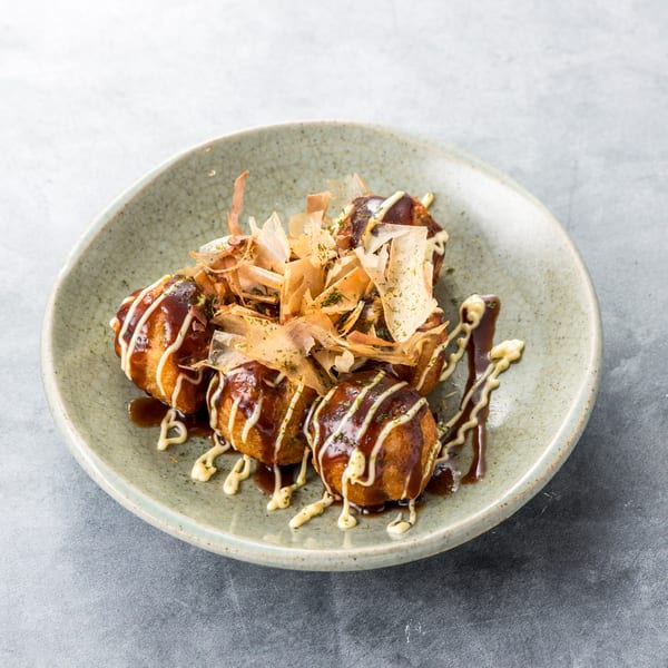 A plate of Takoyaki, fried octopus balls, drizzled with sauce, mayonnaise, and bonito flakes.