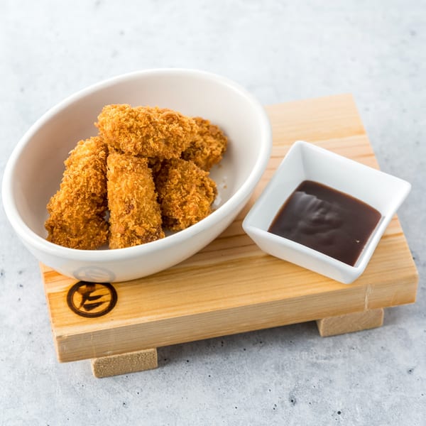 Crispy fried chicken pieces in a white bowl with a side of dark dipping sauce on a wooden board.