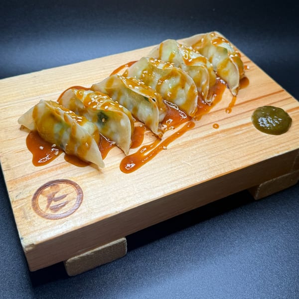 Tanto Gyoza and Ramen Bar's gyoza, drizzled with sauce and sesame seeds, on a wooden board.