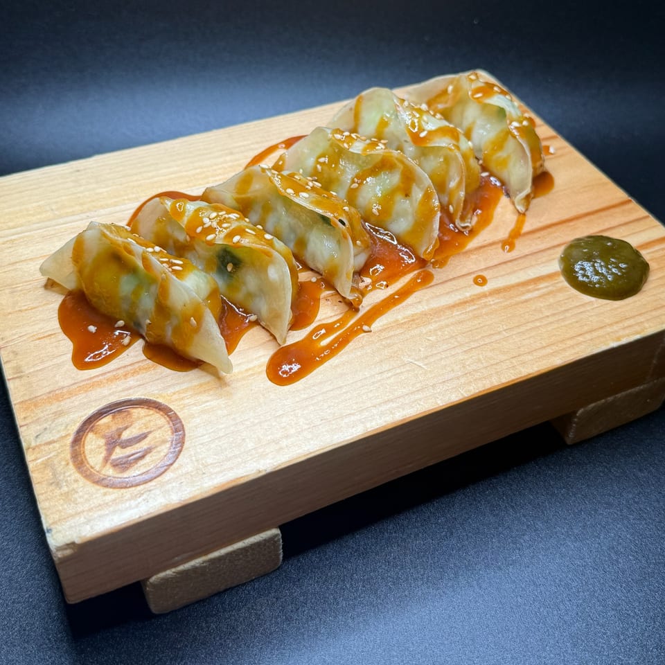 Tanto Gyoza and Ramen Bar's gyoza, drizzled with sauce and sesame seeds, on a wooden board.