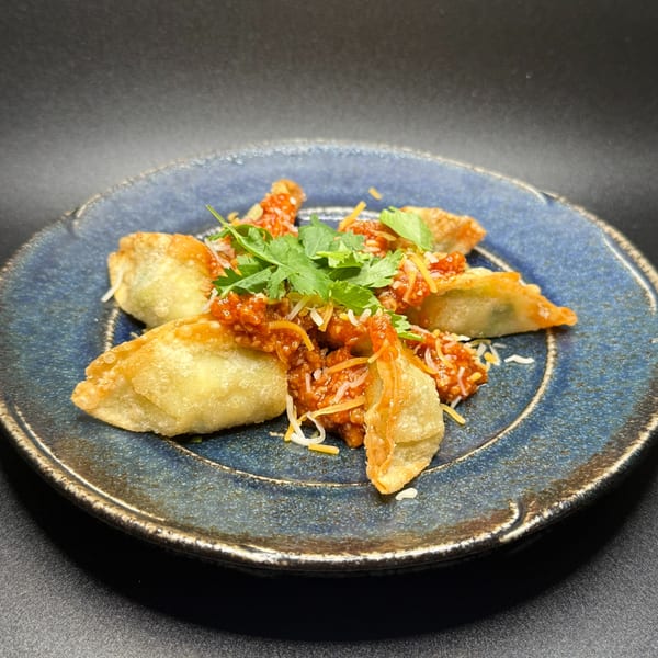 Crispy fried gyoza topped with a savory red sauce, shredded cheese, and fresh cilantro on a blue plate.